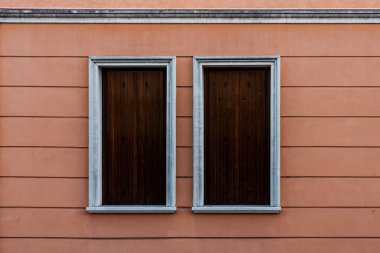 Pembe bir binanın ahşap tahtalarıyla kaplı iki beyaz pencere.