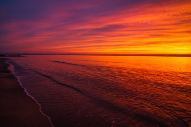 Güzel bir gün batımını yansıtan kumlu bir sahilin deniz manzarası.