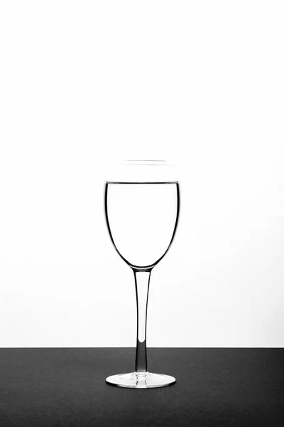白を背景に黒の表面にワイングラスの水の垂直閉鎖 — ストック写真
