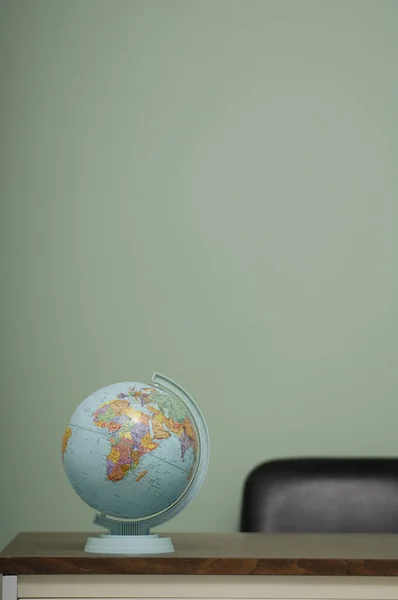 A Vertical shot of the globe on the table and green wall in the background