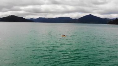 Dağlarla çevrili mavi sakin bir gölde kano yapan insanların güzel manzarası.