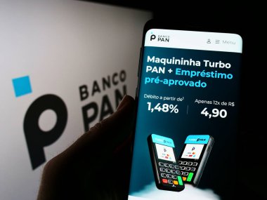 Cep telefonunda Brezilya ticari bankası Banco Pan SA 'nın internet sayfası olan kişi logonun önünde ekranda. Telefon ekranının merkezine odaklan.
