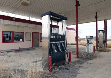 Paslı pompaları ve yıkık dökük binaları olan eski terk edilmiş bir benzin istasyonunun yan görüntüsü.
