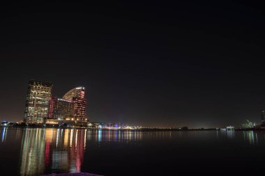 Gece Dubai, BAE 'deki deniz kıyısında aydınlatılmış şehir binaları.