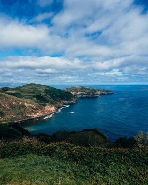Okyanusun dikey görüntüsü, dağlık sahil ve güneşli bir günde manzaralı bulutlar.