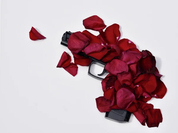 A top view of a gun covered in red rose petals on a white background