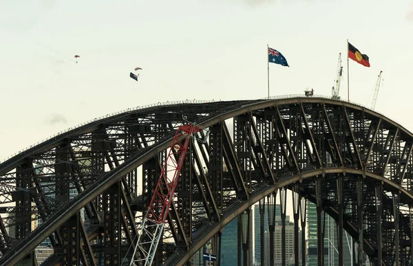 an Australian Flag and Aboriginal Flag over Sydney Harbour Bridge with Parachuters.