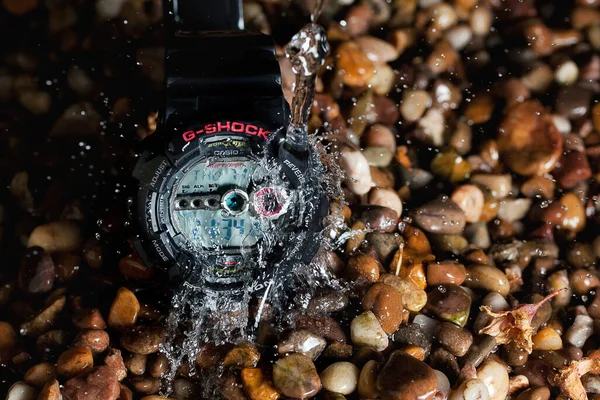 Çakıl taşlarıyla çevrili G-Shock dijital saati ve su sıçraması.