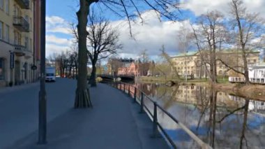 İsveç, Orebro 'daki binaları yansıtan Svartan nehri boyunca yürüyen bir pov.