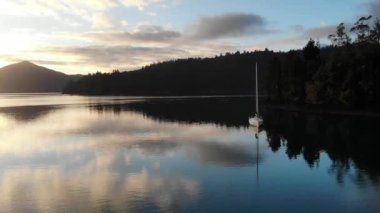 Gün batımının manzaralı bir görüntüsü. Ağaçların ve dağların siluetleriyle dolu bir göl boyunca.