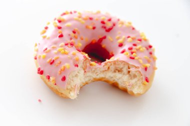 Beyaz arka planda küçük bir ısırıkla pembe bir çöreğin yakın plan çekimi.