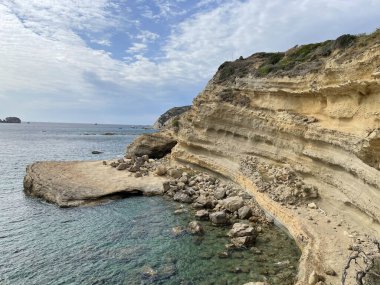 Bulutlu bir gökyüzünün altındaki kayalıklarla çevrili güzel bir deniz manzarası.