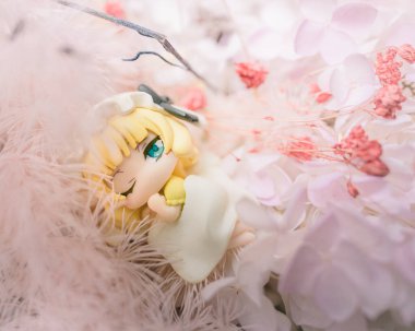 Çiçeklerle dolu bir yatakta uyuyan küçük bir anime kız heykelciğinin yakın çekimi.