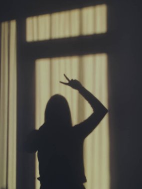 Duvara yansıyan bir kadının silüet fotoğrafı elini V işaretini yaparken gösteriyor.