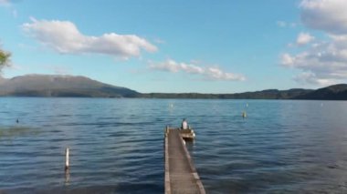 Yeni Zelanda 'daki Tarawera Gölü ve yaya köprüsünde oturan birinin üzerinden geçen bir hava görüntüsü.