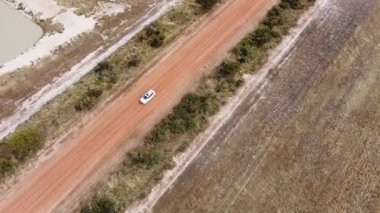 Çiftçilik arazilerinde bir yolda giden beyaz bir arabanın kuş bakışı görüntüsü