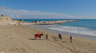 Sicilya 'daki Avola plajında bir grup insanın yanında ata binen bir kadın.