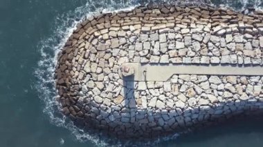 Portekiz 'deki kayalık bir rıhtımın sonundaki kırmızı ve beyaz deniz fenerinin havadan görünüşü.