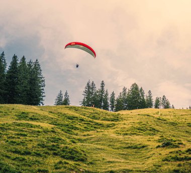 Bulutlu gökyüzünün altında dağdan uçan bir paraglider.