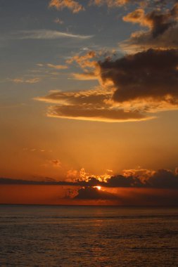 Deniz üzerindeki bulutların arkasında nefes kesici bir günbatımının dikey çekimi.