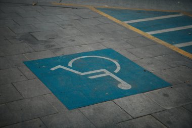Bir sokağın kenarındaki mavi engelli park levhasının yakın çekimi.