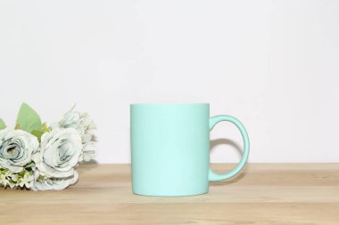 Mavi bir kupa ve çiçekler ahşap bir masada beyaz bir duvara karşı