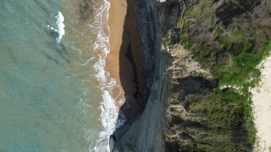 Uçurumların altında turkuaz deniz dalgaları tarafından yıkanan huzurlu kumlu bir sahil.