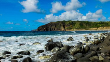 Sahildeki kayaların yeşil dağlara karşı manzarası güneşli bir günde bulutlu mavi gökyüzü.