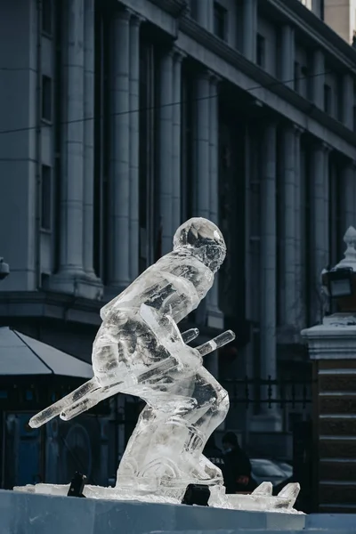 A vertical shot of an ice sculpture of a male with fighting sticks under a blue sky