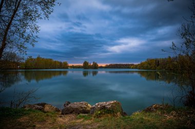 Almanya 'nın Bavyera kentindeki sulara yansıyan ağaçlarla çevrili güzel bir günbatımı.
