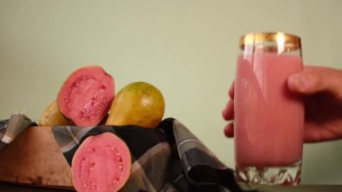 Bir kase guava meyvesi ve bir dilim guava taze sıkılmış meyve suyunun yanında.