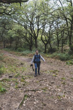Ormanda yürüyen kameralı genç bir adam.