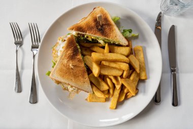 Tavuklu beyaz tabakta sandviç ve patates kızartması manzarası.