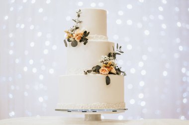 Üç katlı beyaz düğün pastası süslenmiş.