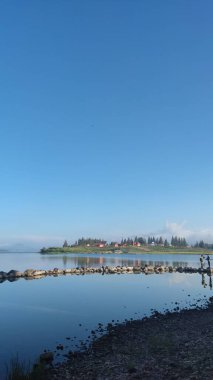 Sakin denizin dikey görüntüsü, kıyı boyunca kayalar mavi gökyüzünün altındaki tepedeki köy evlerinin arka planı.