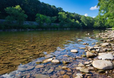 Ağaçlarla çevrili bulutlu bir gökyüzünde büyük kayaları olan bir nehir.