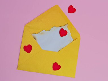 Üzerinde eski kağıtlar ve pembe arka planda kalp şeklinde çıkartmalar olan sarı bir zarf.