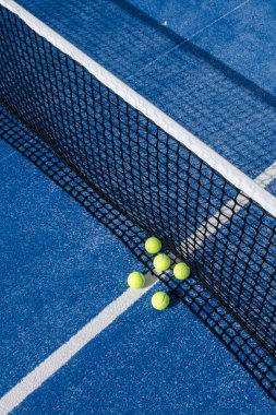 Mavi bir raket tenis kortunda, ağdaki birkaç raket tenis topunun yakın çekimi.