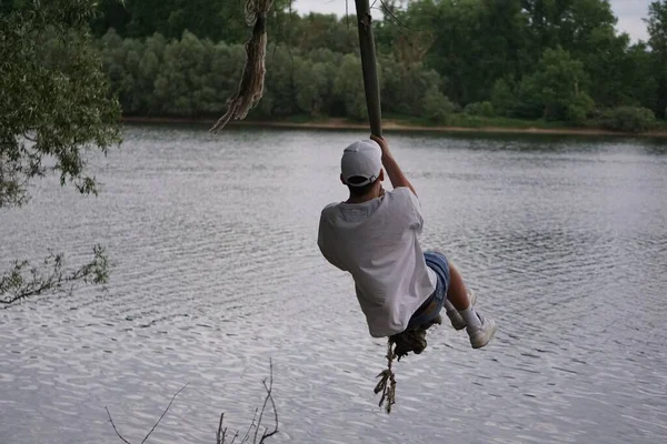 一个年轻男子用绳子在绿树成荫的湖水上荡秋千的背景 — 图库照片