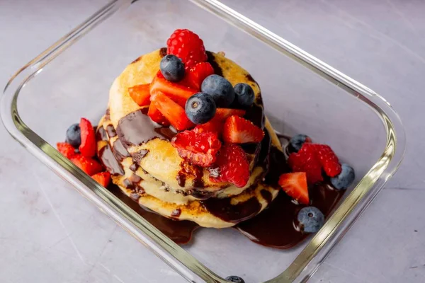 A closeup shot of fluffy pancakes with chocolate syrup with raspberries, strawberries and blueberries
