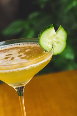 Portakal renkli bir kokteyl ve ahşap bir masanın üzerinde salatalık sosu.