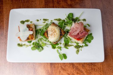 Tabakta servis edilen jambonlu ve yeşillikli mini sandviçlerin üst görüntüsü.