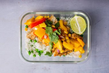 Şeffaf bir tabakta pilav ve sebzeyle hazırlanmış tavuğun üst görüntüsü.