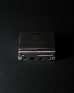 Siyah bir Gameboy, siyah arkaplan ile izole bir şekilde masada ilerliyor.