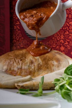 Yeşilliklerle süslenmiş bir köftenin üzerine dökülen sosun dikey yakın çekimi.