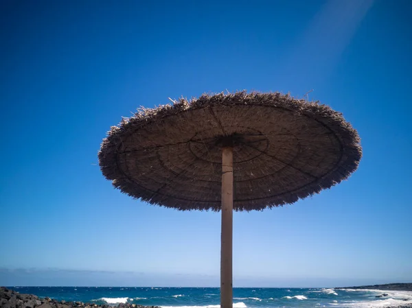 青い海と雲一つない空に対してわらのビーチの傘のローアングルショット — ストック写真