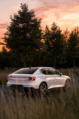 Kar beyazı bir Volvo Polestar 2 'nin günbatımında bir kır yolunda performans paketi ile dikey çekimi.