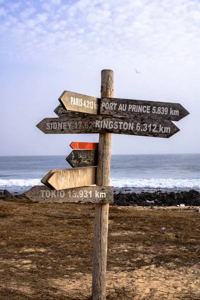 A closeup of wooden direction signs on a road with a view of a sea under the blue cloudy sky