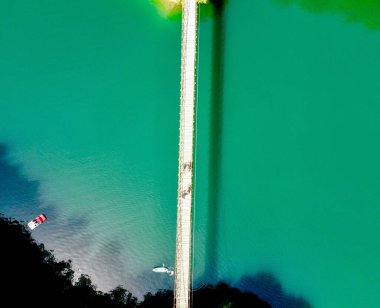 Belluno 'daki Lac du Corlo Gölü üzerindeki uzun bir köprünün insansız hava aracı görüntüsü.