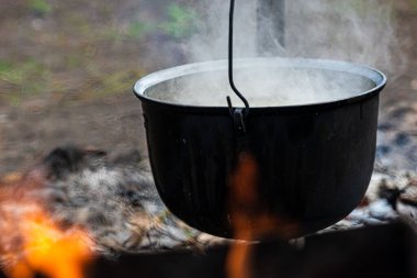 Bir kamptaki şenlik ateşinde, demir bir kasede kaynayan suyun yakın plan çekimi.